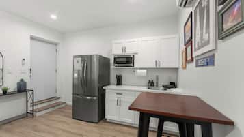 Una cocina moderna con armarios blancos, un refrigerador de acero inoxidable, un microondas y una mesa de madera.