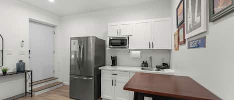 A modern kitchen with white cabinets, a stainless steel refrigerator, a microwave, and a wooden table.