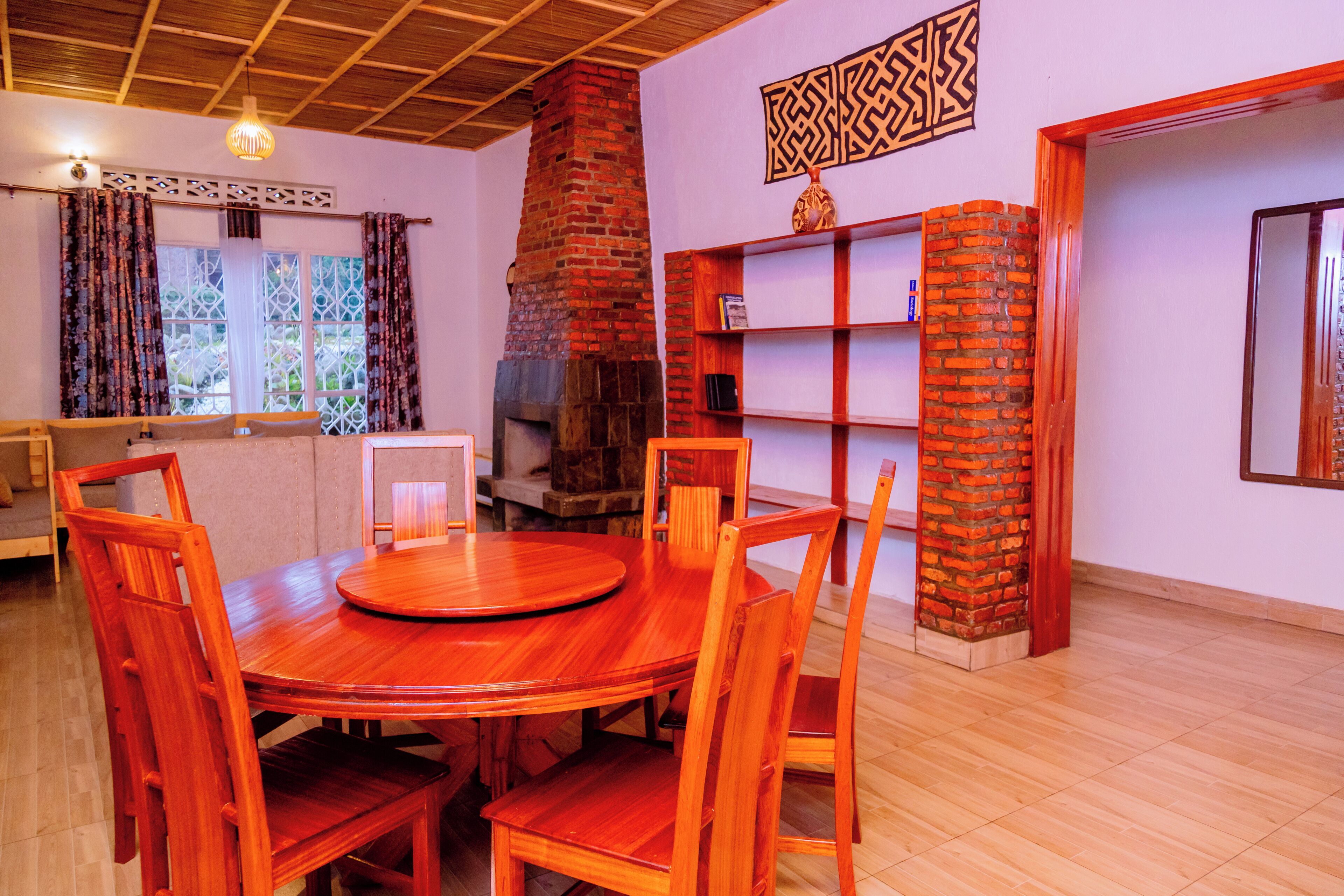 A dining area with a round wooden table and chairs, a brick fireplace, and a bookshelf.