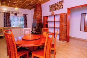 A dining area with a round wooden table and chairs, a brick fireplace, and a bookshelf. - Future4kids Kinigi Guest House By Isange Paradise Resort (Musanze)
