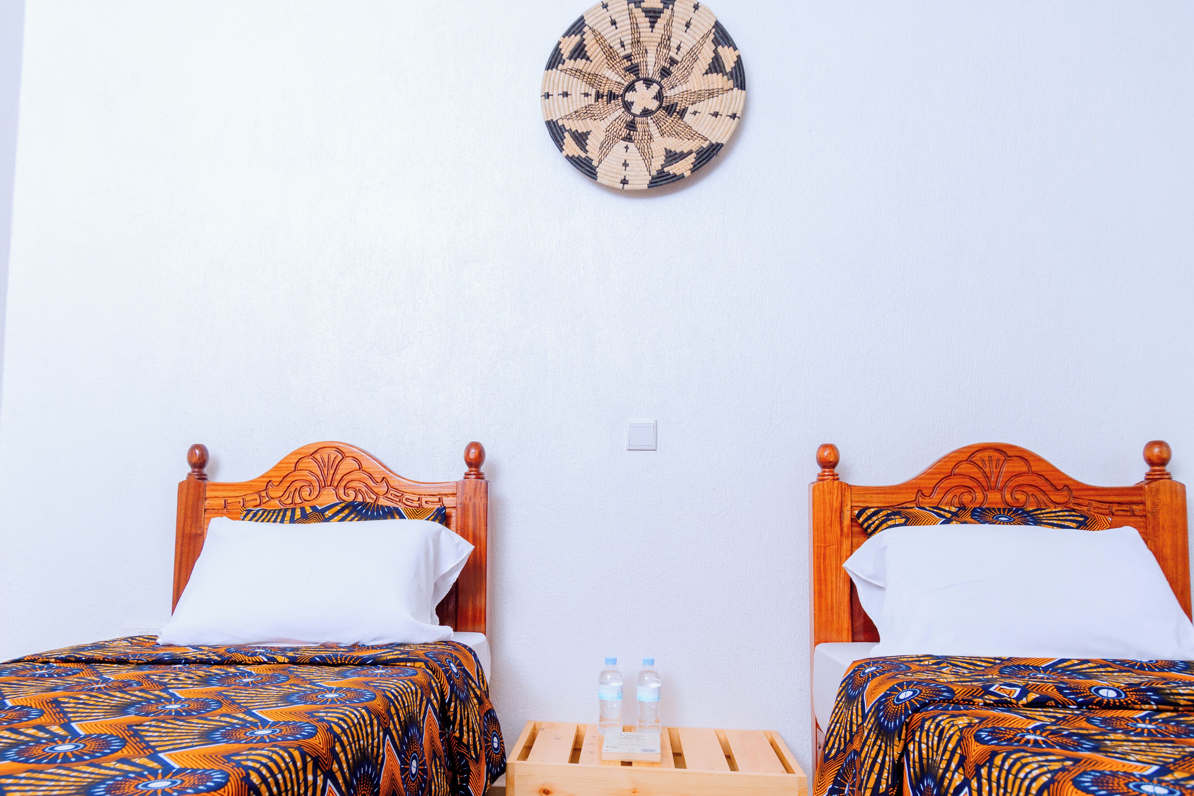 Two wooden beds with matching headboards, a wall-mounted decorative plate, and a wooden nightstand with two water bottles.