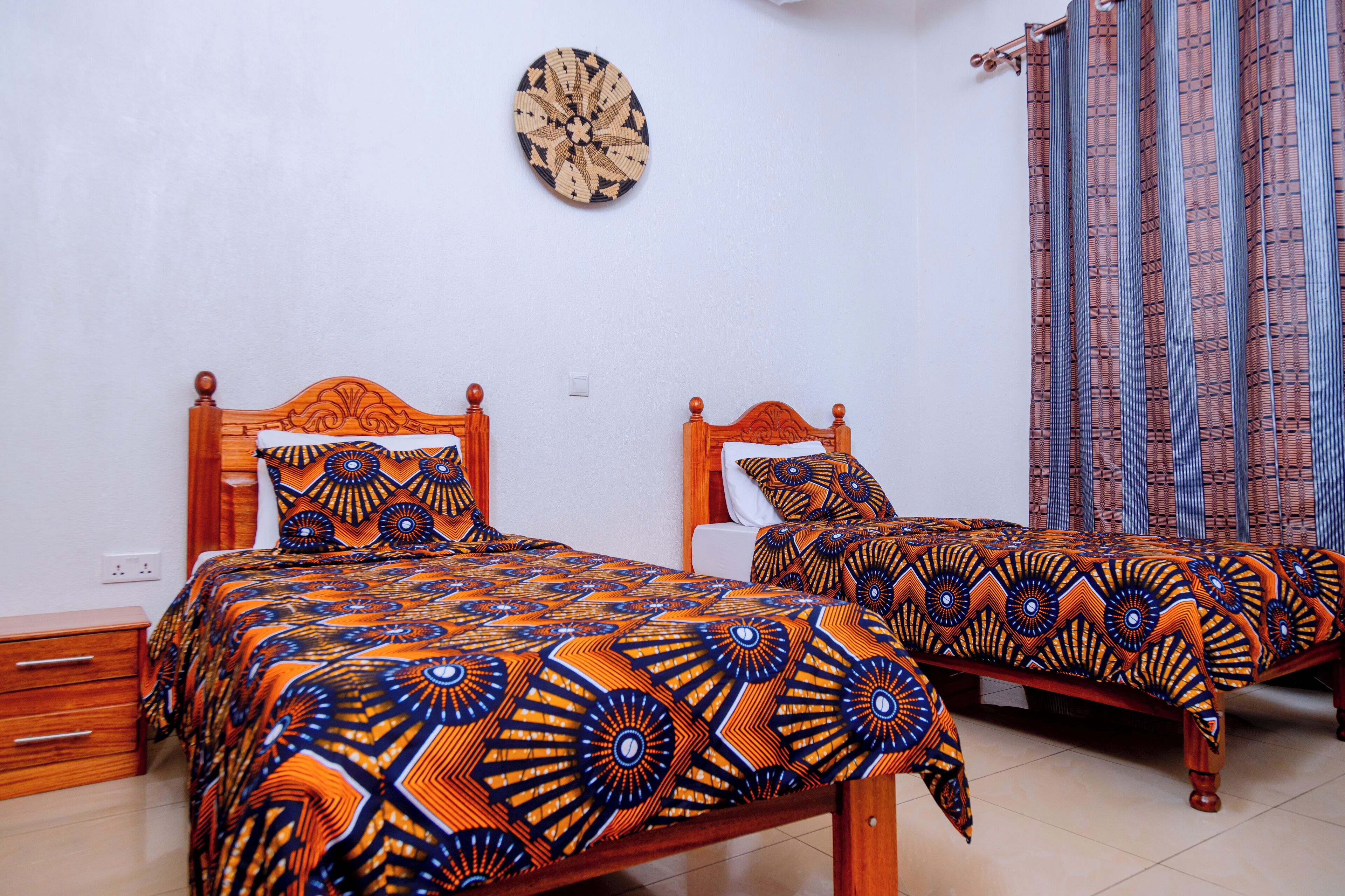 Dos camas de madera con cabeceras y pies de cama a juego, un plato decorativo en la pared y una cortina estampada.