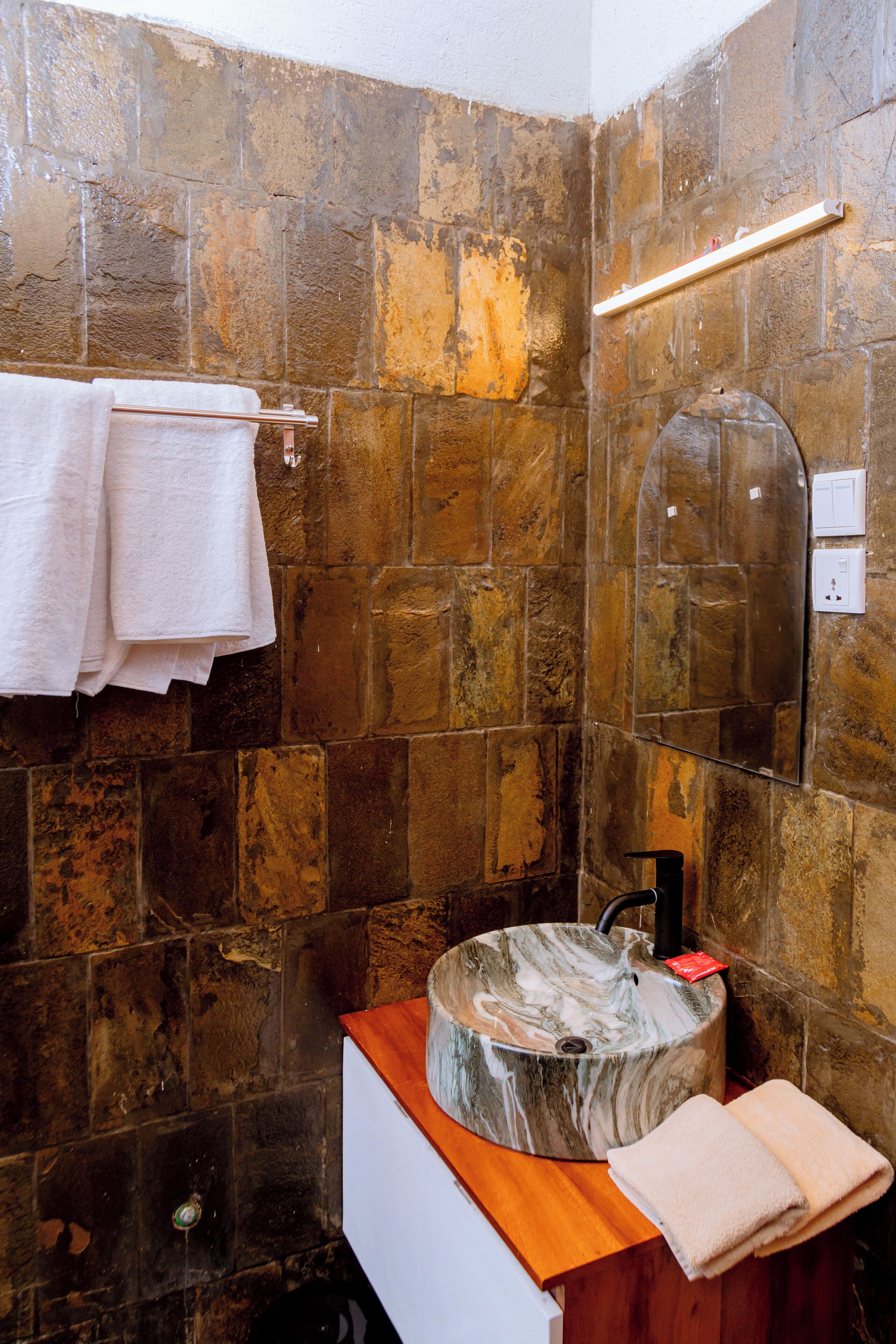A bathroom with stone walls, a wooden vanity, a marble sink, and a towel rack.
