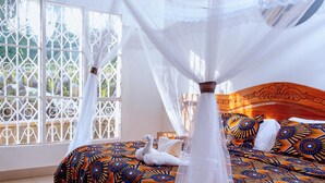 A bed with a canopy, patterned bedding, and a view through a window with decorative metal grilles. - Future4kids Kinigi Guest House By Isange Paradise Resort (Musanze)