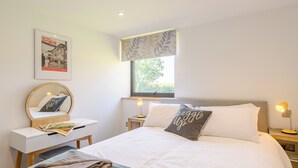Un dormitorio ordenado con cama, mesitas de noche, un escritorio, una silla, una ventana con vistas y un cartel en la pared.