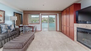 Una sala de estar con sofá, televisión, chimenea y vista a una masa de agua a través de ventanas grandes.