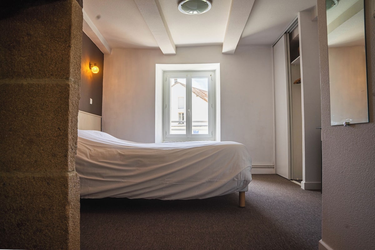 A bedroom with a bed, a window, a door, and a light fixture.