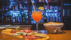 A bar setting with a drink, a cheese board, and a basket of bread. - Logis Hôtel EBEN (Egletons)