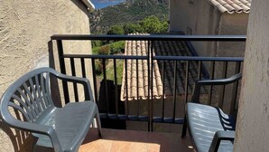 Un balcón con dos sillas de plástico, piso de baldosas y vistas a montañas y un lago.