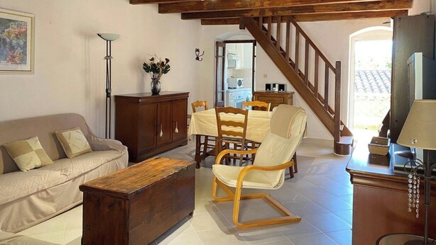 Una sala de estar acogedora con techo de madera, un sofá, una mesa de comedor con sillas, un sillón mecedora y un televisor.