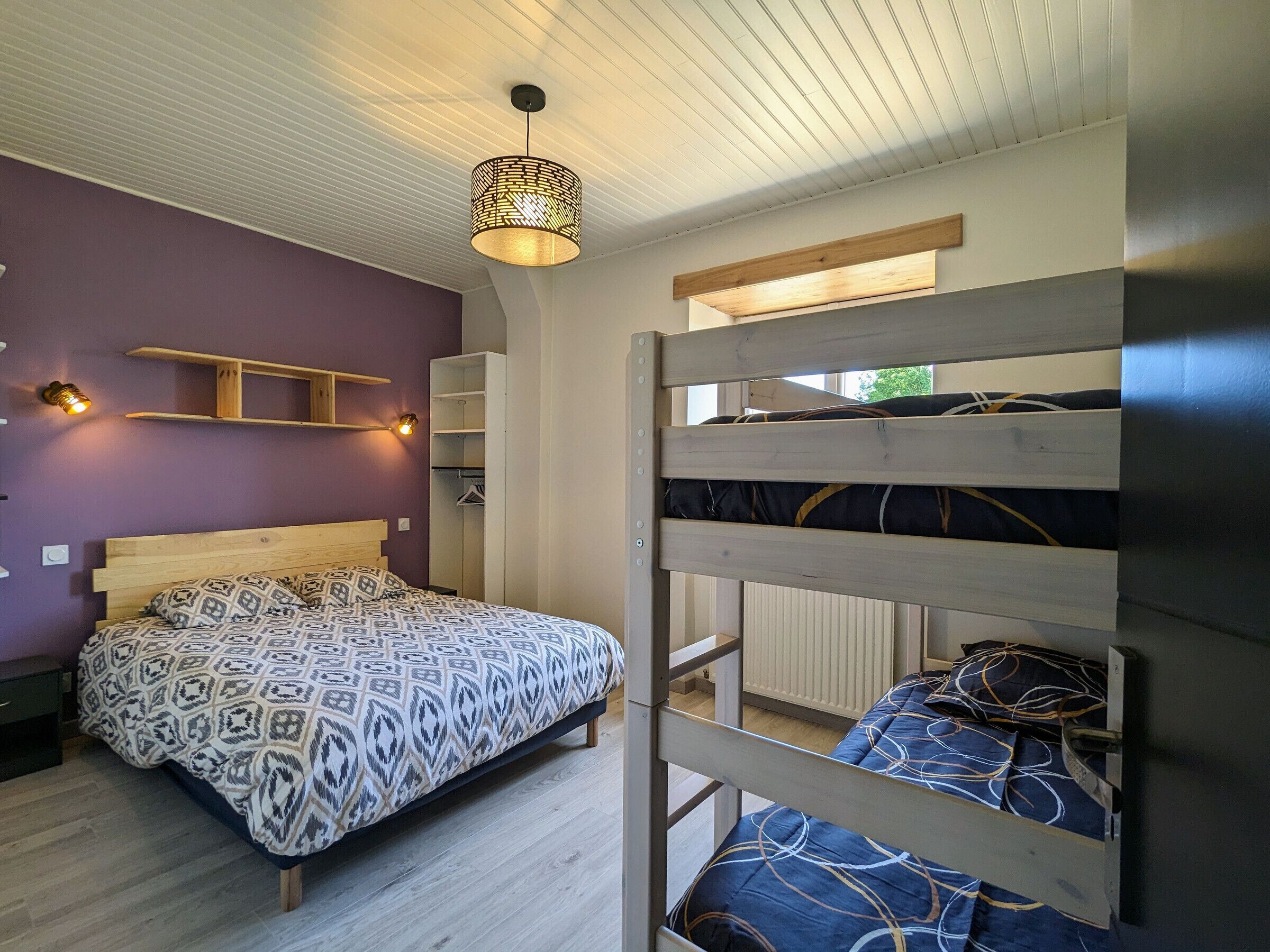 A room with a bunk bed, a single bed, a hanging light fixture, and built-in shelving.