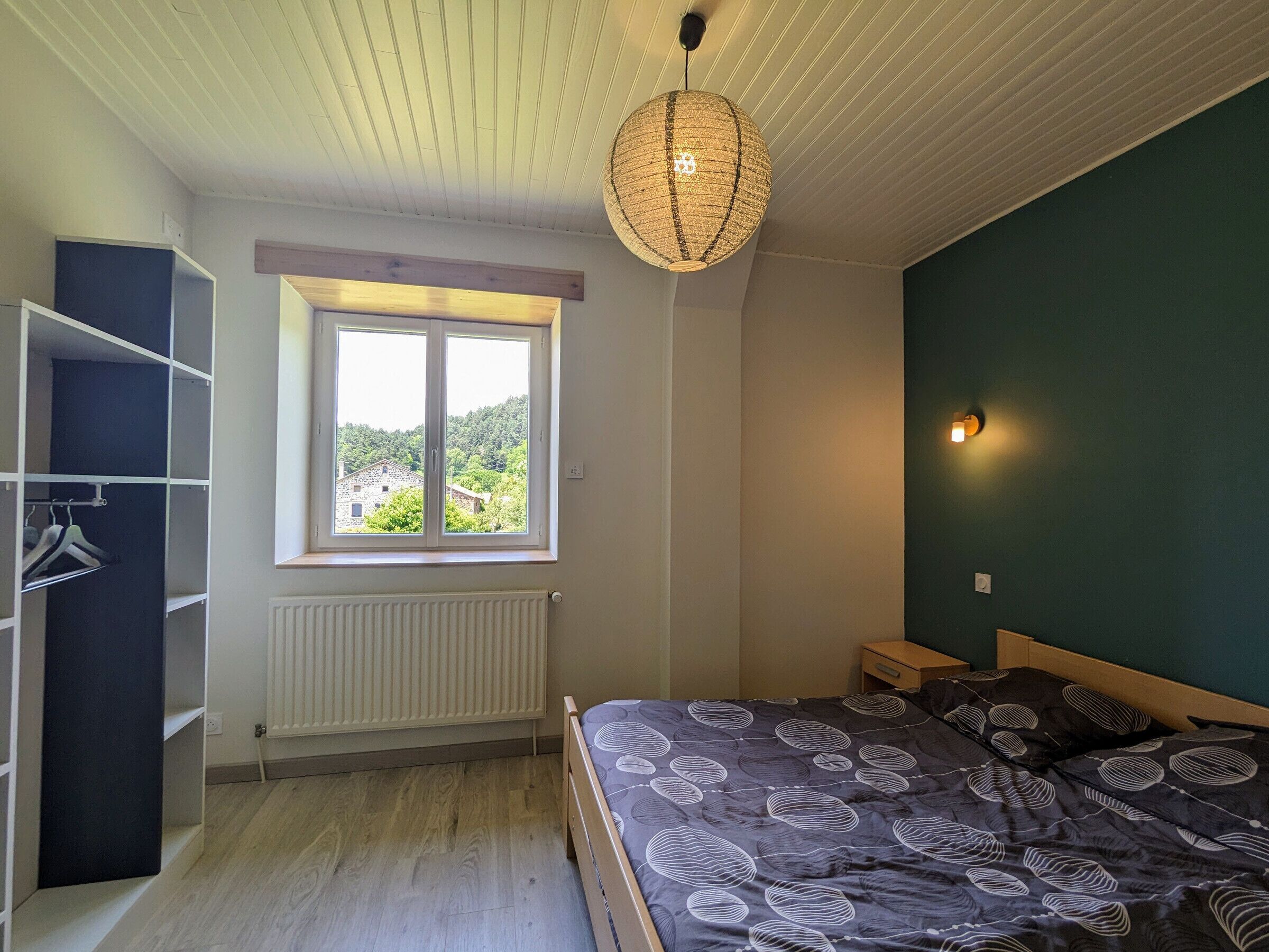 Une chambre à coucher comprenant un lit, une armoire, une fenêtre avec vue, un luminaire suspendu et une applique murale.