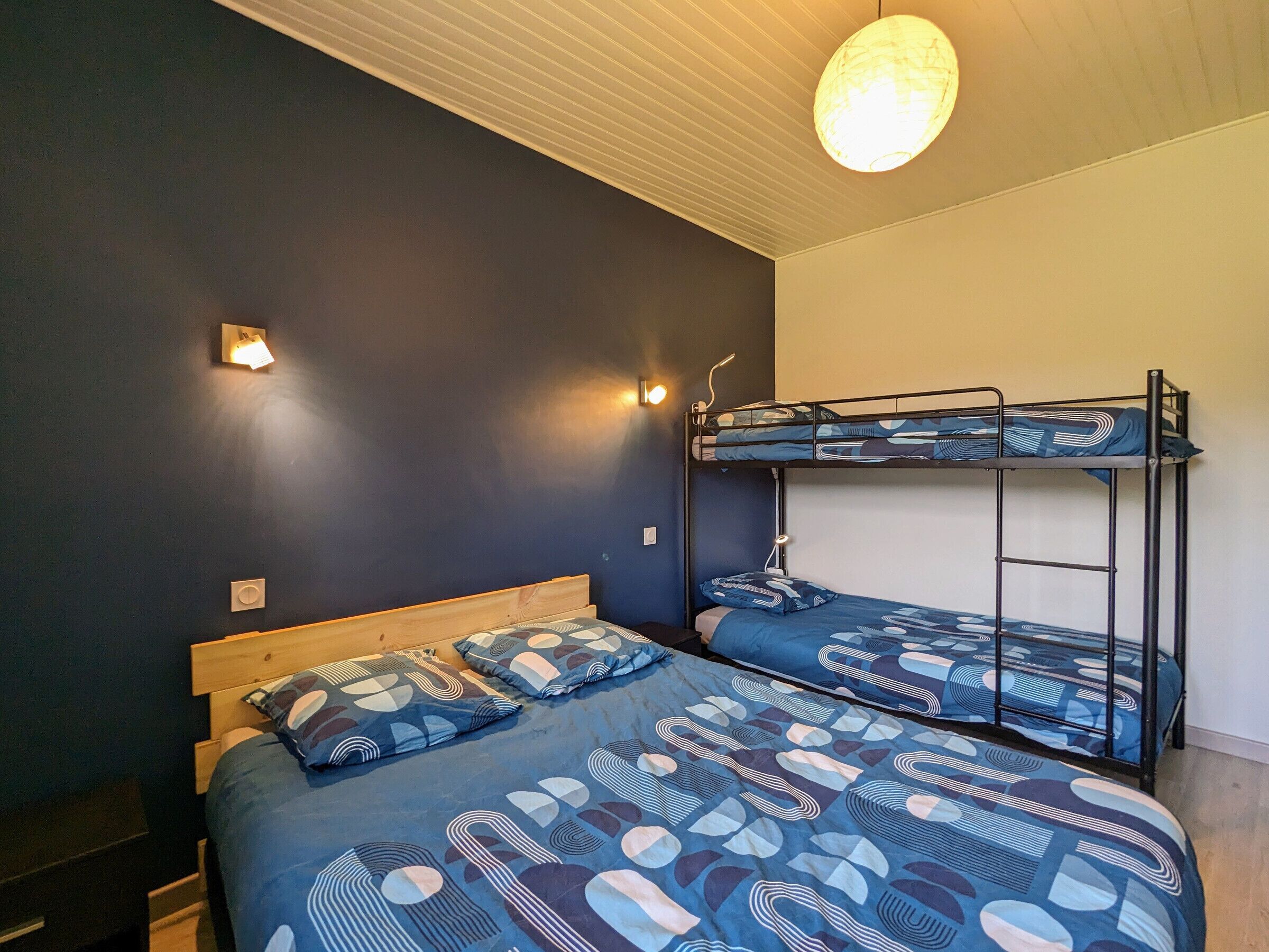 A bunk bed room with a patterned bedspread, two wall-mounted lights, and a ceiling light fixture.