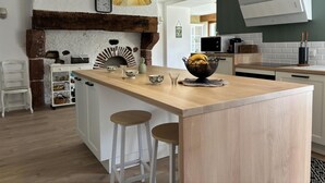 Eine moderne Küche mit einer zentralen Kochinsel, Holzbarhocker, einer hängenden Leuchte und einem Backofen aus Ziegelsteinen.