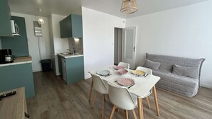 A compact living space with a kitchenette, dining area, and a grey sofa. - Beachside 2-Room Apartment with Private Garage in Saint-Hilaire-de-Riez (Saint-Hilaire-de-Riez)