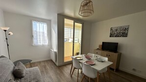 A modern living space with a sofa, dining table, chairs, a TV, and a balcony. - Beachside 2-Room Apartment with Private Garage in Saint-Hilaire-de-Riez (Saint-Hilaire-de-Riez)