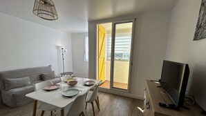 A modern living space with a dining area, a sofa, a TV, and a sliding glass door to the outside. - Beachside 2-Room Apartment with Private Garage in Saint-Hilaire-de-Riez (Saint-Hilaire-de-Riez)