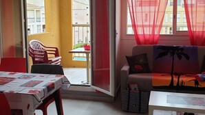 A room with a balcony, a sofa, a table, and a chair. - Charming Air-Conditioned Apartment with Pool & Parking, Close to Port and Beach (Cap d'Agde)