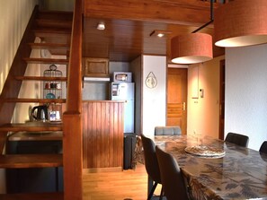 A wooden staircase leading to a kitchen area with a microwave, refrigerator, and wooden cabinets. - Cozy 3-Room Duplex with Mezzanine for Holidays (Font-Romeu-Odeillo-Via)