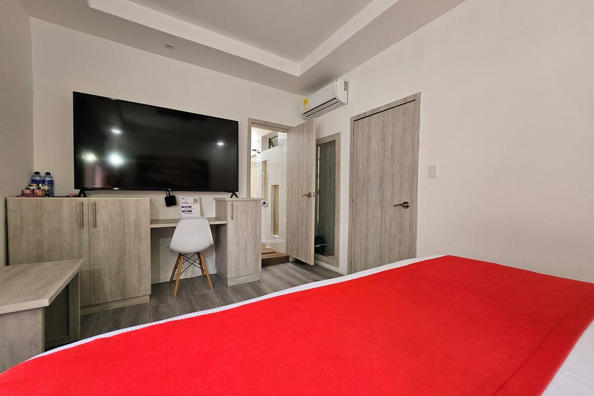 Habitación de hotel con una amplia televisión de pantalla plana, un escritorio con silla, un armario y alfombra roja.