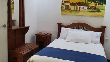 Un dormitorio con una cama, una mesita de noche, un banco de madera, un ventilador de techo y un cuadro en la pared.