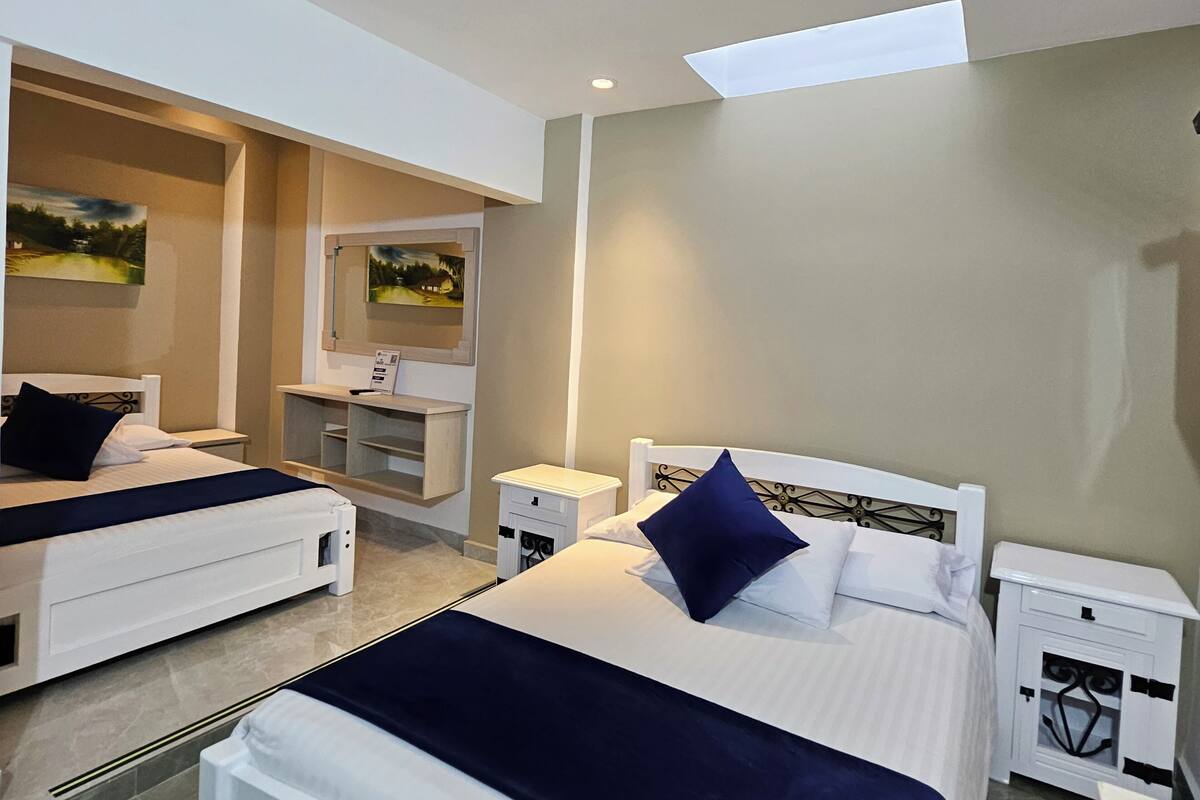 Una habitación de hotel con dos camas, un escritorio, un espejo y un tragaluz.