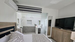 Habitación de hotel con cama, televisión, armario de madera y baño visible a través de una puerta corredera.