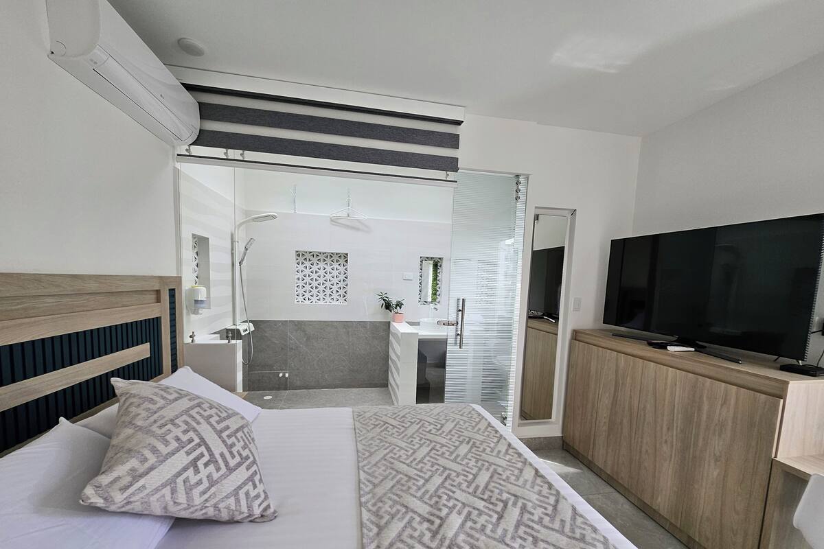 Habitación de hotel con cama, televisión, armario de madera y baño visible a través de una puerta corredera.