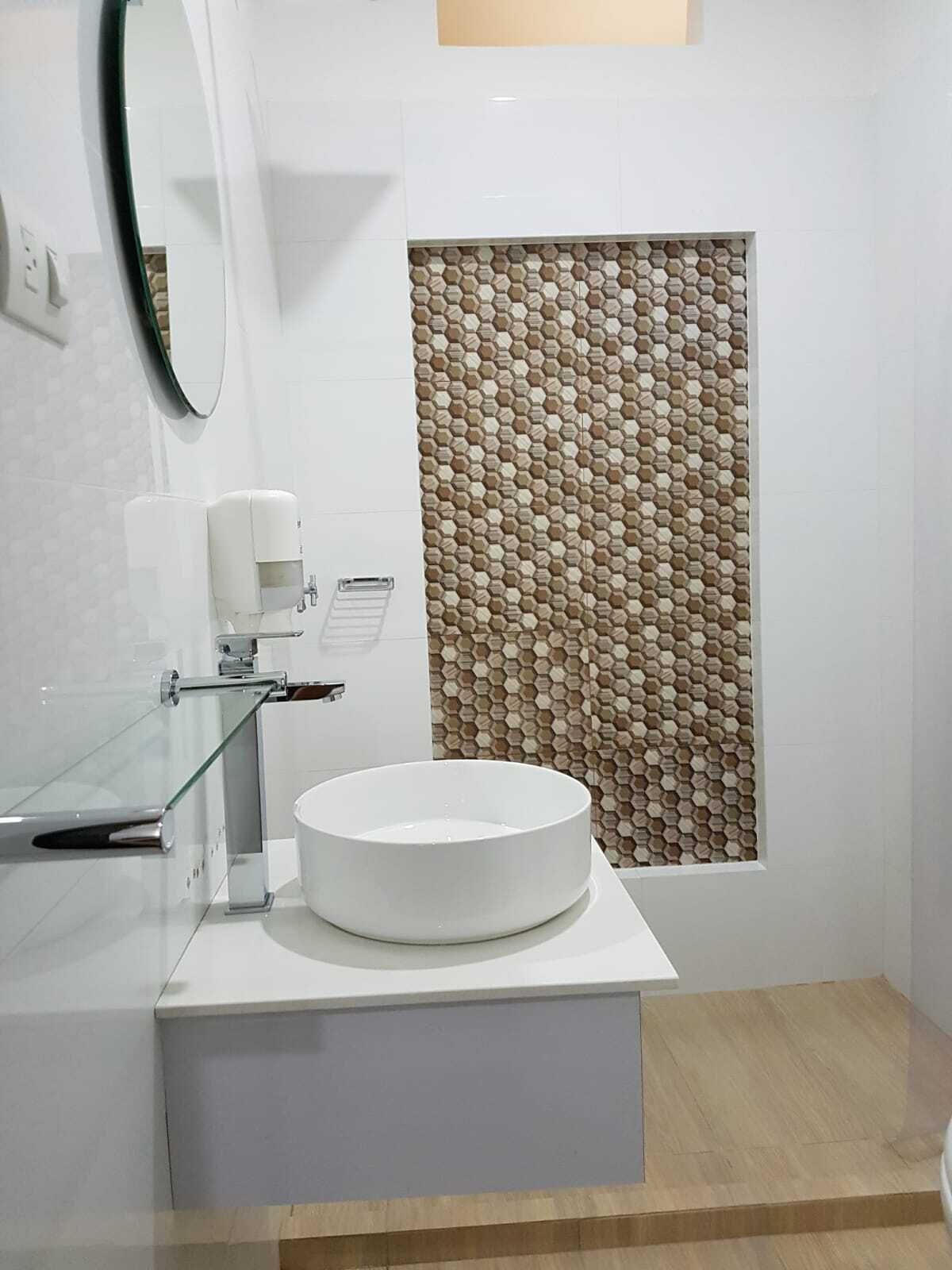 A modern bathroom with a round white sink, a glass shower enclosure, and a hexagonal patterned wall.