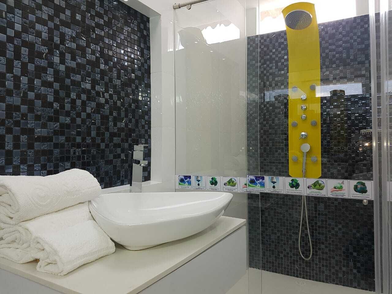A modern bathroom with a white sink, a glass shower enclosure, and a yellow showerhead.