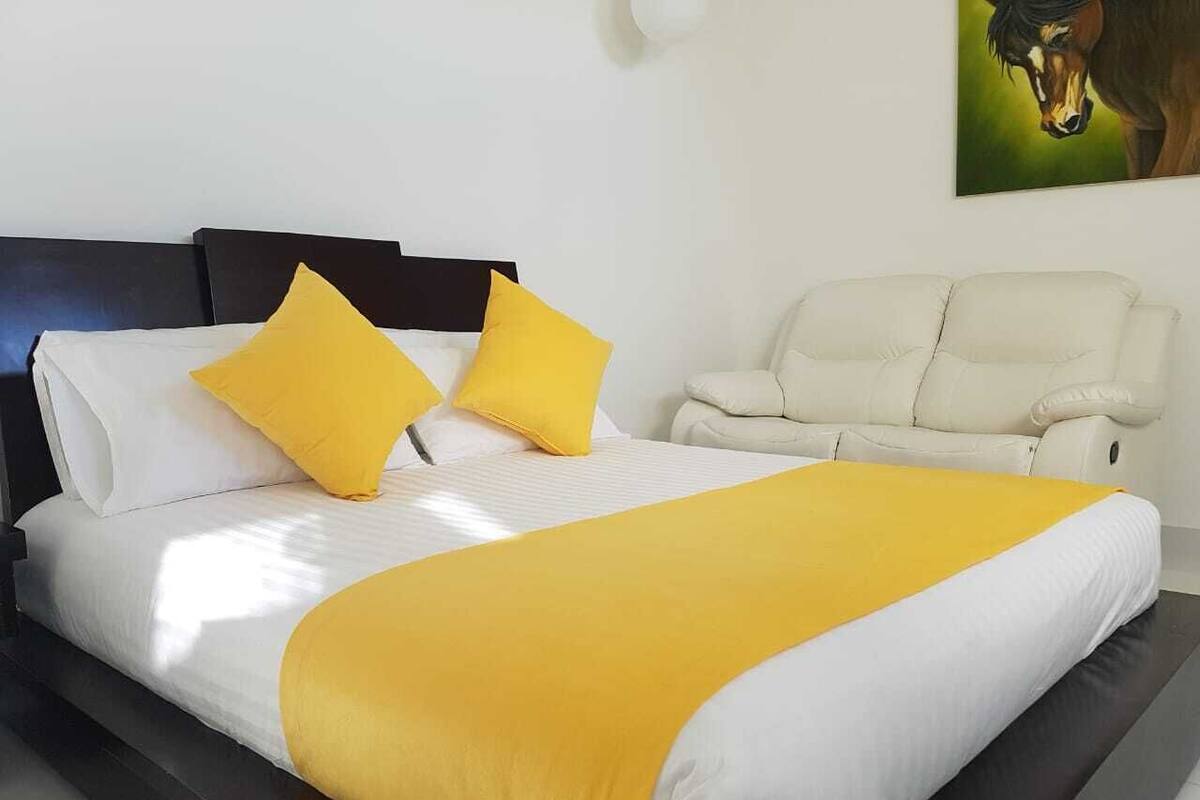 Una cama con ropa de cama blanca y amarilla, un cabecero negro y una manta amarilla.