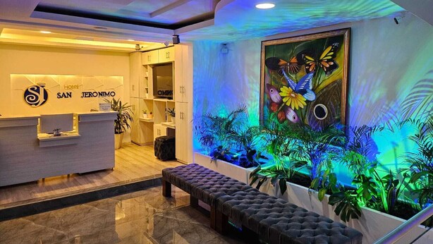 Zona de recepción de un hotel con diseño moderno, que incluye un mostrador de recepción, un área de descanso con un banco y una pared con un mural de mariposas colorido.