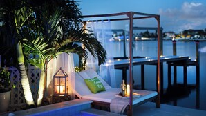 A poolside lounge with a canopy, a candle, and a bottle of champagne. - Dolphin Bay Bungalow – Waterfront Pool, Kayaks, & Walk to Indian Rocks Beach (Indian Rocks Beach)