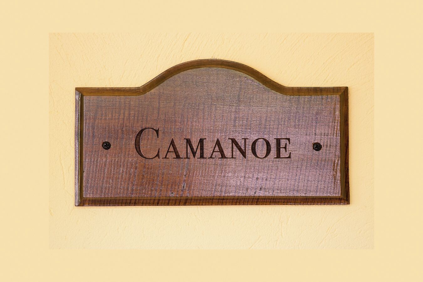 A wooden nameplate with the name "CAMANOE" mounted on a wall.