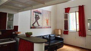 A living room with a black leather sofa, a small table with a lamp, a potted plant, and a large abstract painting on the wall. - Delightful Loft in Pigneto - to Colosseum in 10 minutes (Roma)