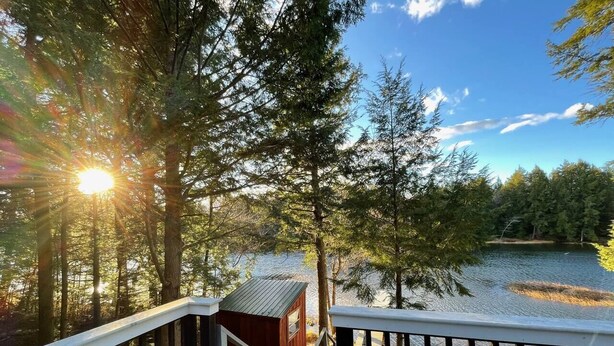 Une terrasse en bois avec une petite cabane, donnant sur un lac entouré d’arbres.