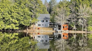 Une maison au bord d’un lac, avec un quai et un petit abri de jardin.