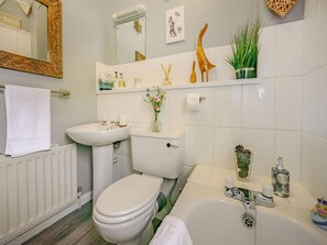 A bathroom with a toilet, sink, and bathtub. There are decorative items on the shelves, including a vase with flowers and a wooden sculpture.