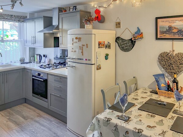 Une cuisine moderne avec des meubles gris, un réfrigérateur blanc et un coin repas avec une table mise pour deux personnes.