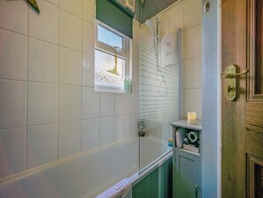 A bathroom with white tiled walls, a window with frosted glass, a shower, and a wooden door. - 1 bedroom accommodation in Keswick (Keswick)