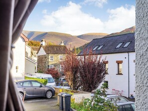Une rue résidentielle bordée de maisons, avec des voitures garées et une vue sur des collines.