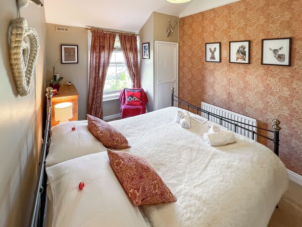 A neatly made bed with floral pillows, a radiator, and framed animal pictures on the wall. - 1 bedroom accommodation in Keswick (Keswick)