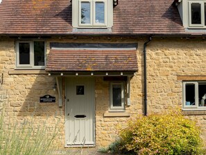 A stone cottage with a white door, a small porch, and a sign reading "HoneySuckle Cottage." - Stylish Cottage | Peaceful Rural Retreat - Pass The Keys (Somerton)