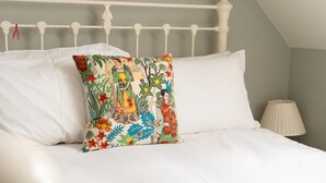 A bed with white linens and a colorful pillow featuring a tropical print.