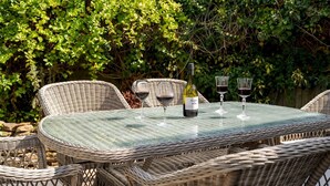 A wicker table with four chairs, a bottle of wine, and two wine glasses.
