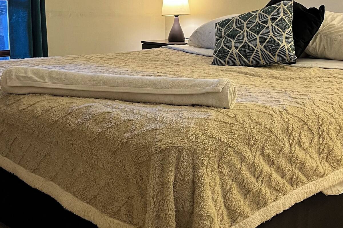 A neatly made bed with a fluffy white blanket, a patterned pillow, and a bedside lamp on a nightstand.