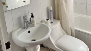 A bathroom with a toilet, sink, mirror, towel, shower curtain, and a window. - Fast Track SCL AirPort (Santiago)