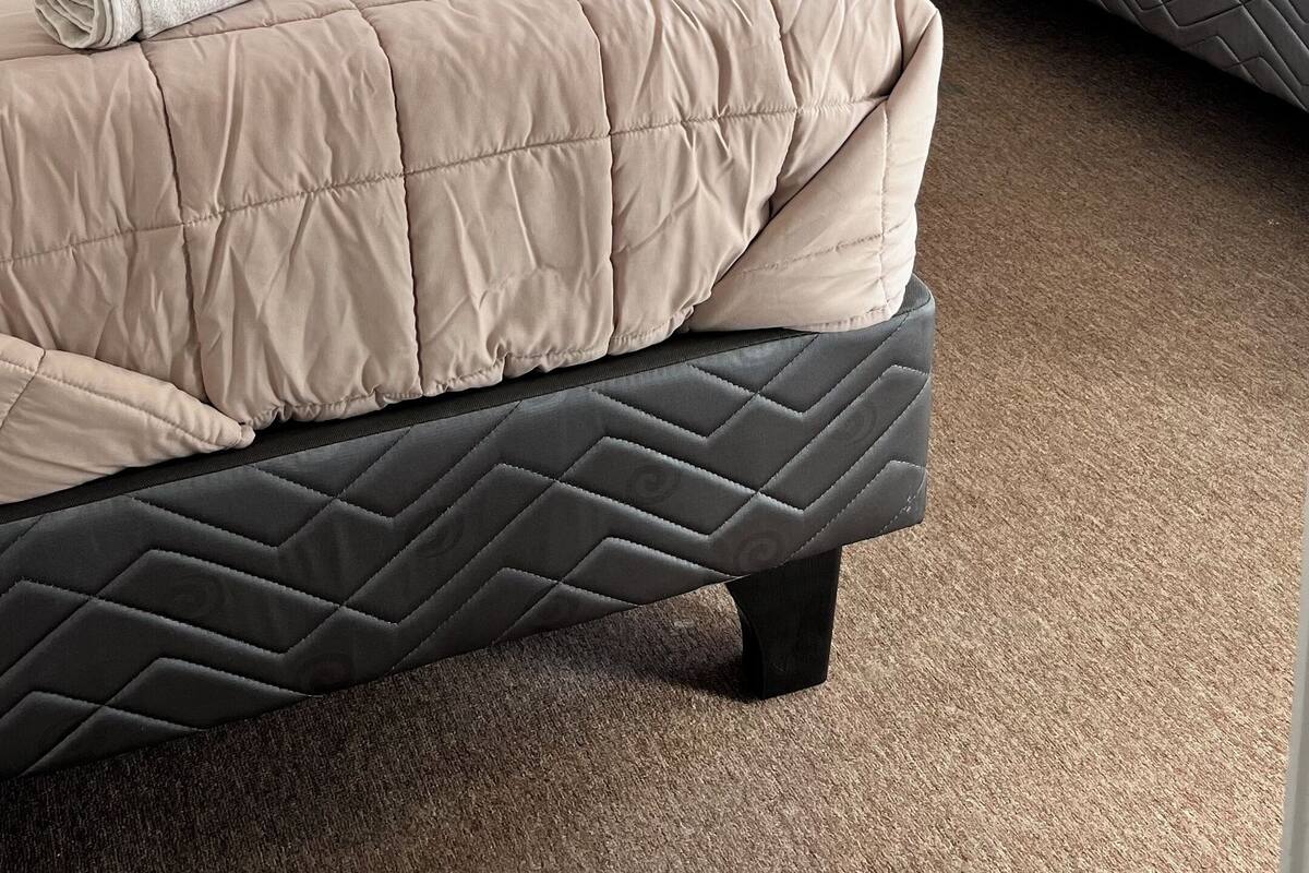 A bedroom with two beds, each with a beige quilted bedspread and white pillows. There is a small bedside table with a lamp between the beds.