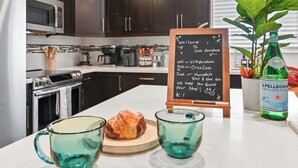 A kitchen counter with a chalkboard menu, two green glass cups, a croissant, and a bottle of Pellegrino water. - Tropical Toucan Retreat w/ Pool (Pompano Beach)