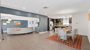 A modern kitchen with dark cabinets, a stainless steel refrigerator, and a dining area with a table and chairs. - Tropical Toucan Retreat w/ Pool (Pompano Beach)